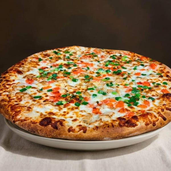 A whole pizza with white sauce, chicken, diced tomatoes, and green onions on a white plate.